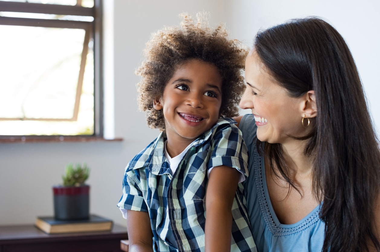 Female foster parent laughing with foster child in living room.